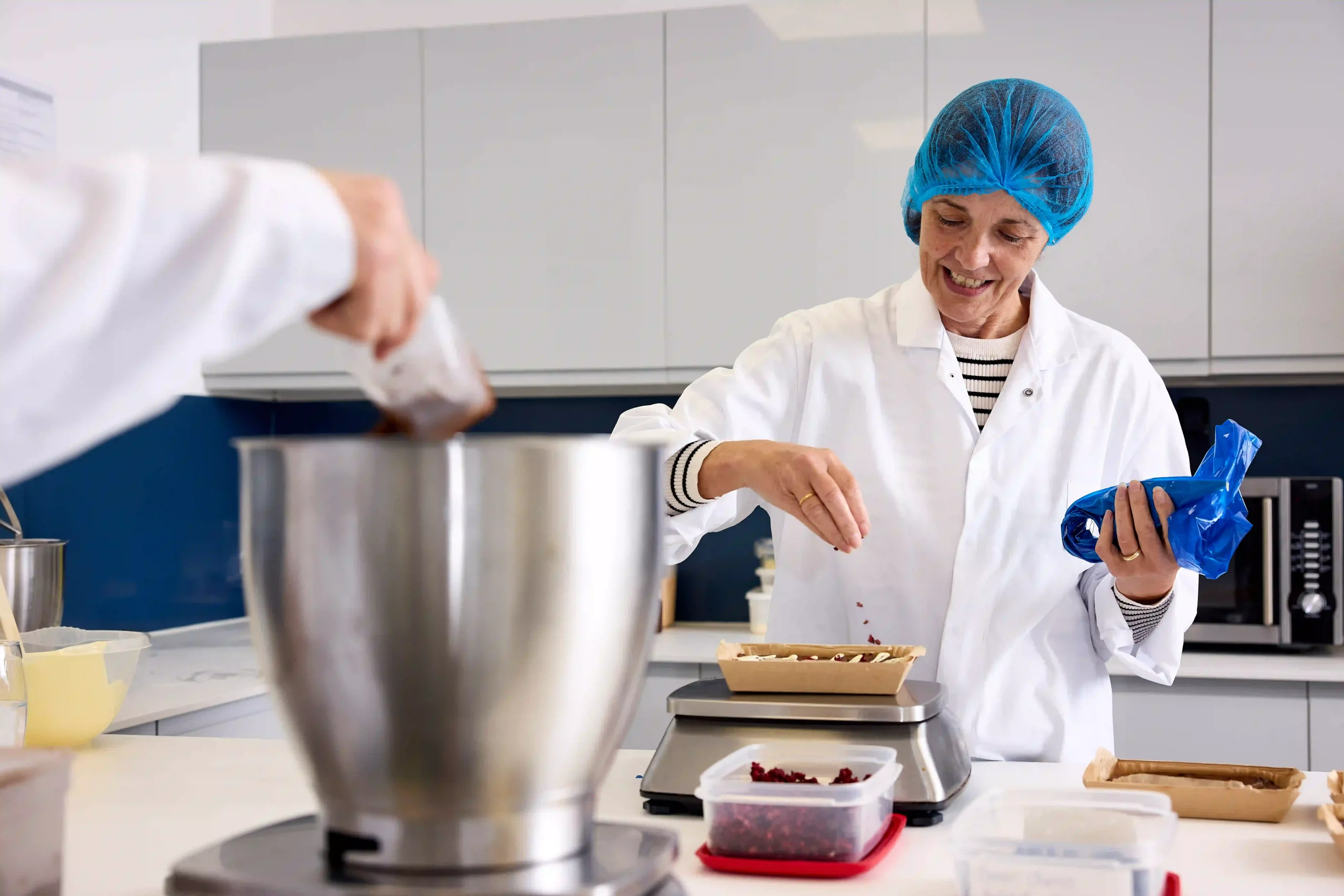 An NPD baker scatters raspberries onto a brownie. In the foreground a baker  puts cocoa powder into a metal bowl
